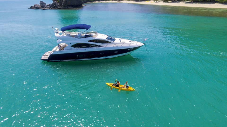 Two people in yellow kayak in front of large white yacht by island in blue ocean