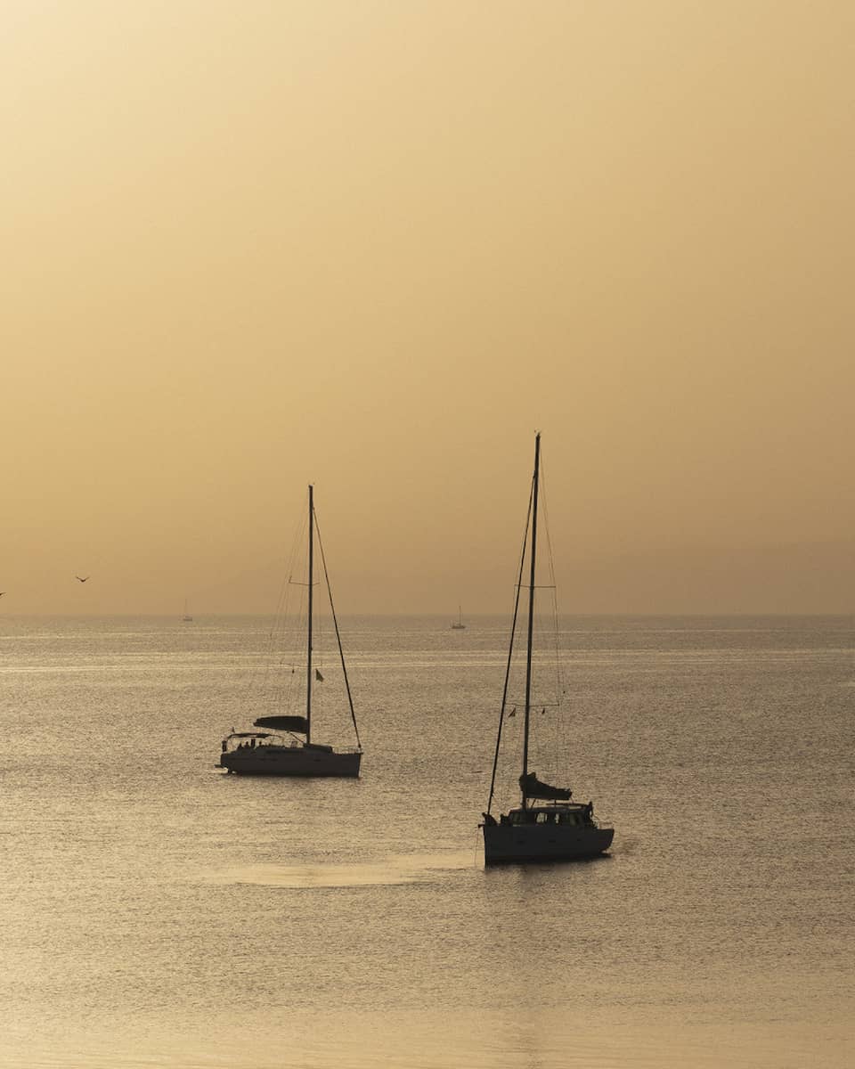 Silhouette of two sailboats at dusk on ocean cruising Greek isles.