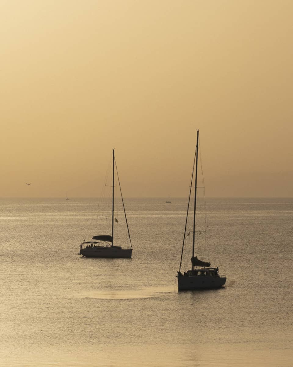 Silhouette of two sailboats at dusk on ocean cruising Greek isles.