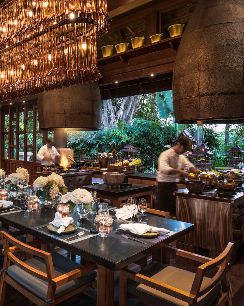 Large dining table under long rectangular crystal chandelier in Rim Tai restaurant, chefs in background