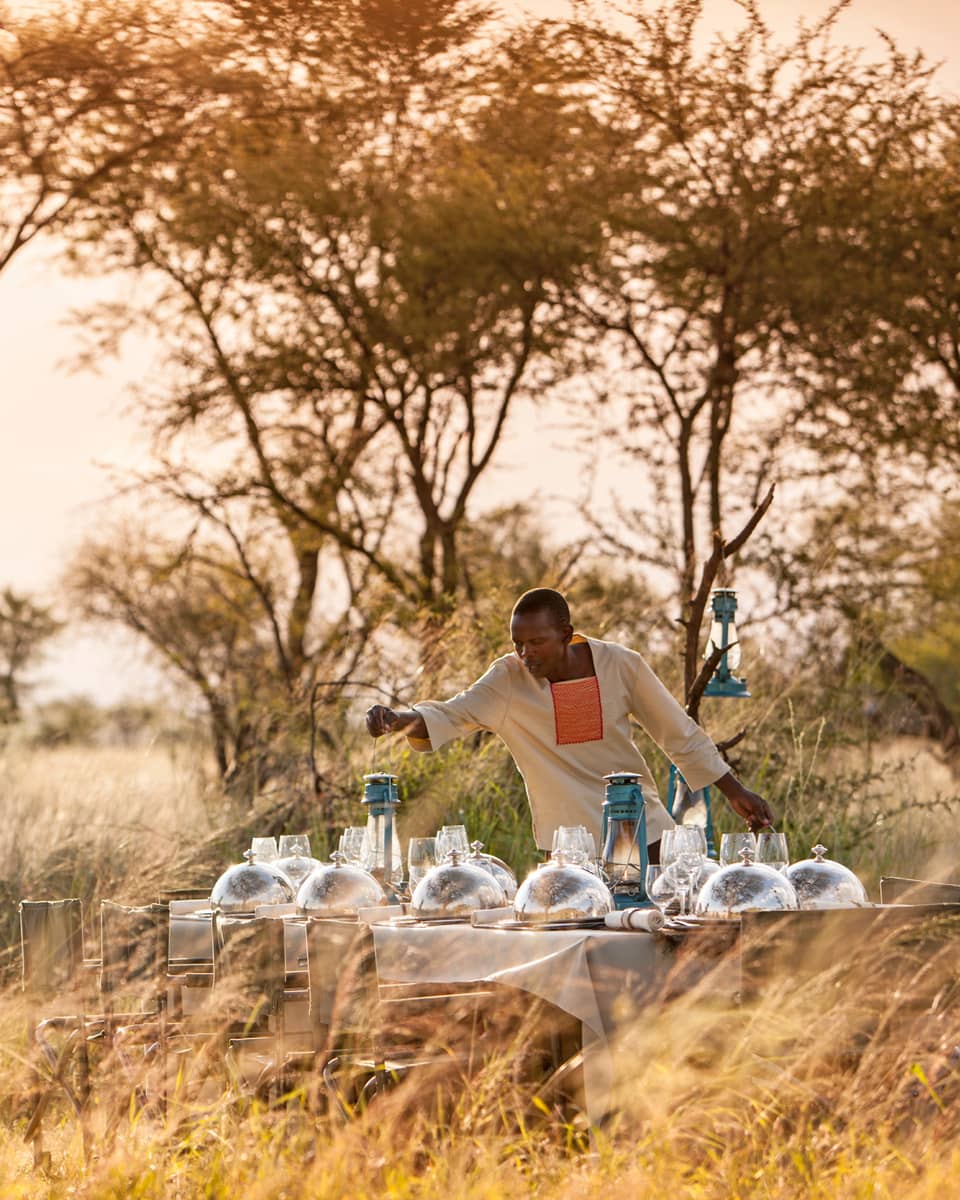 Hotel staff places lantern on long dining table with silver dome planets in grassy field