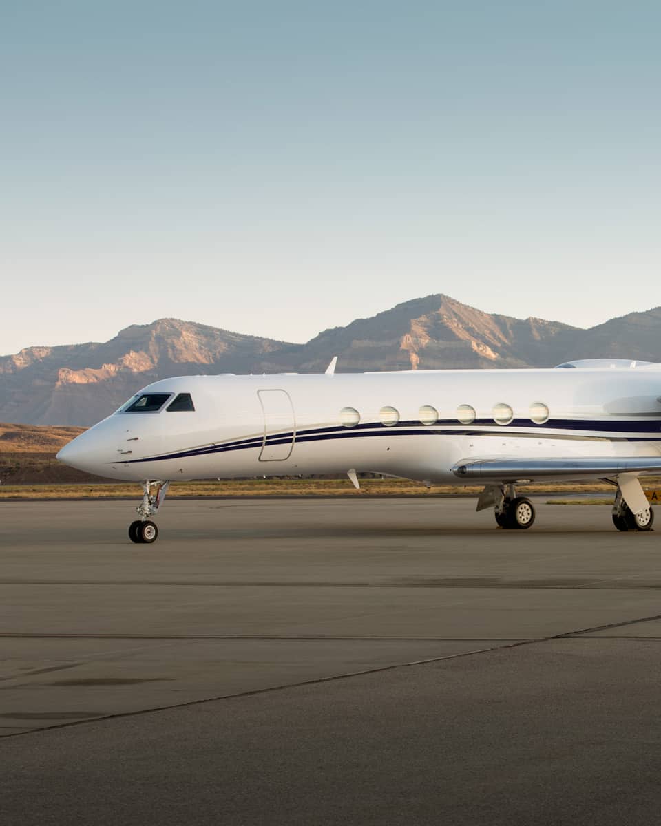 Private jet parked on a runway with mountain range in the background.