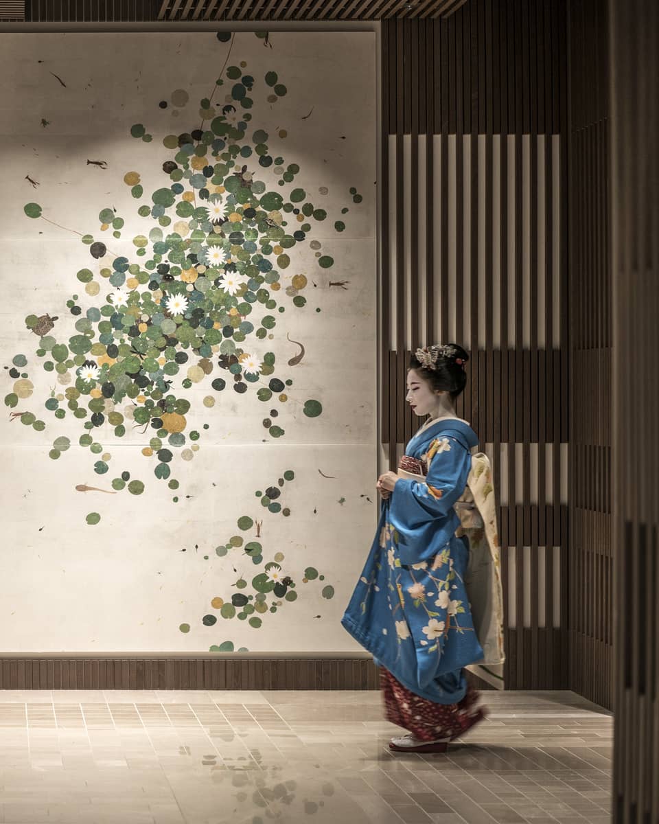 Person in a blue kimono with floral patterns standing in front of a wall decorated with a botanical art piece at Four Seasons