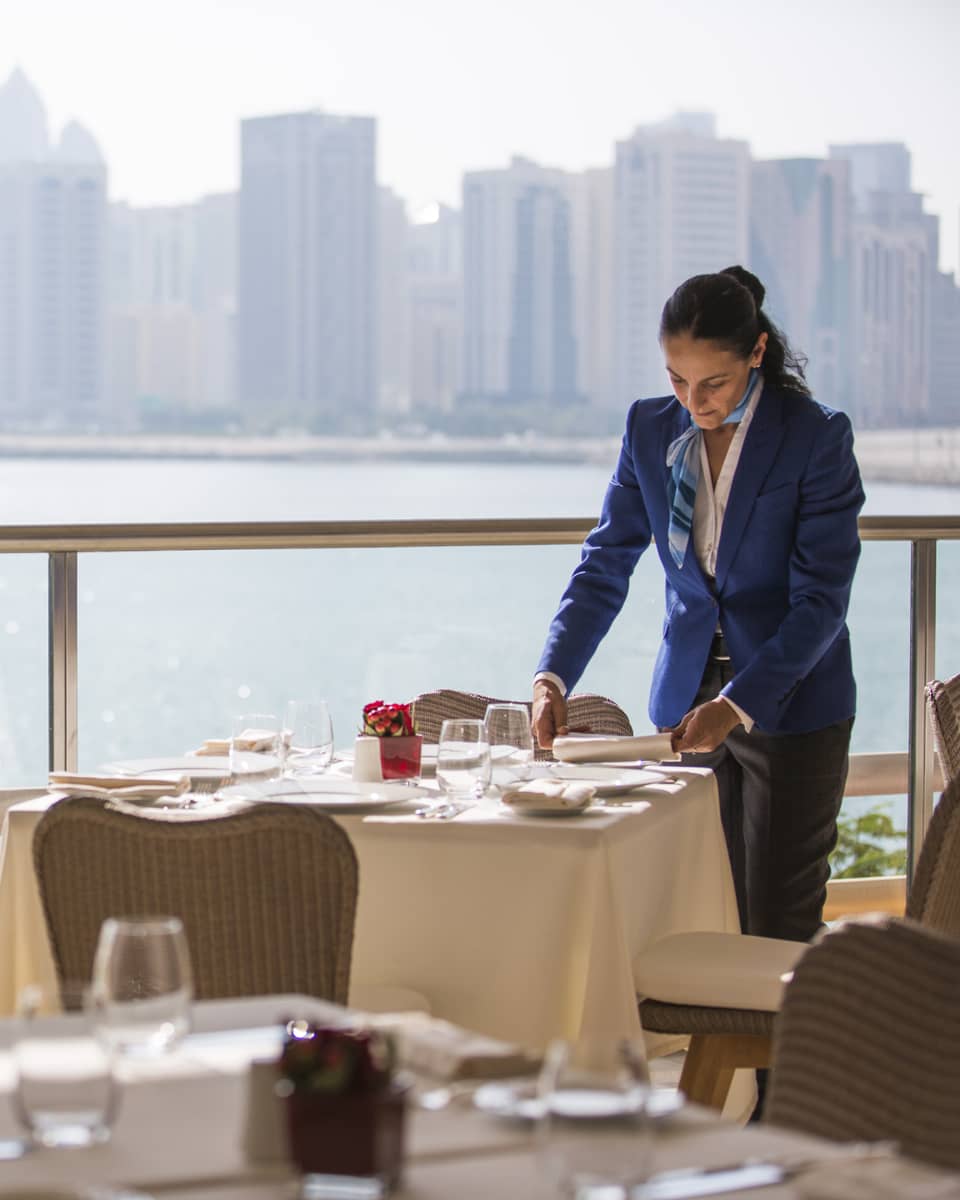 A four seasons staff setting an indoor Cafe Milano table overlooking the water