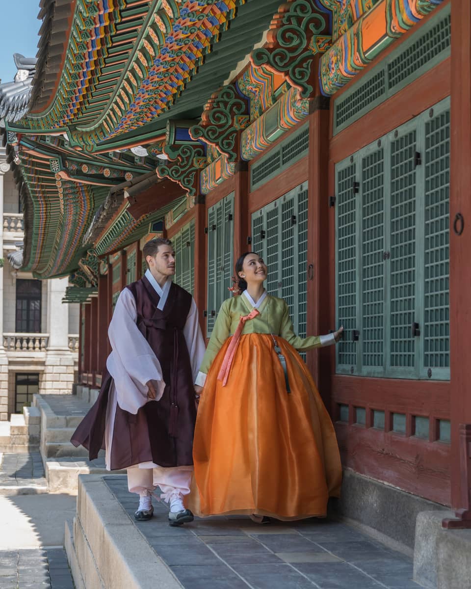 Man and woman in traditional Korean attire walk along the wall of a local palace