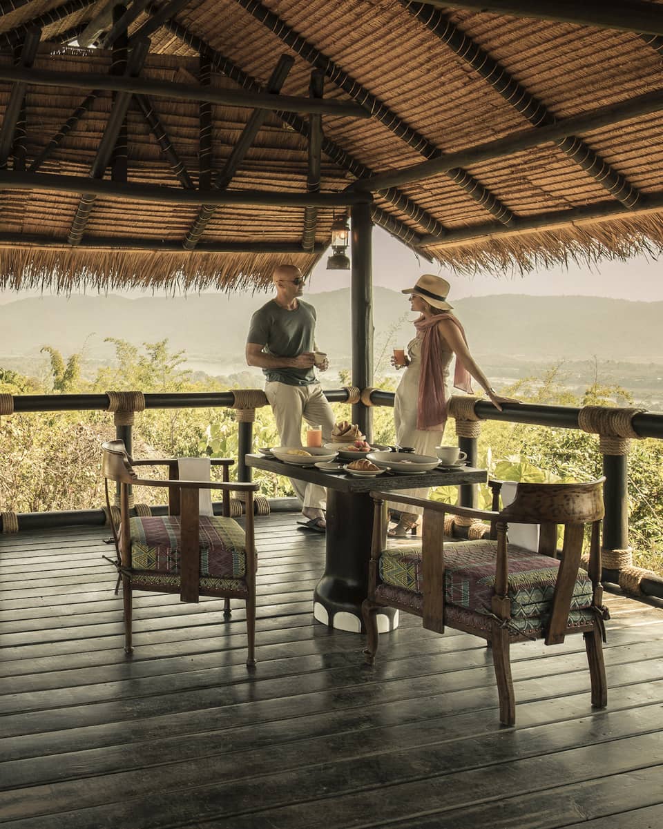 A couple sitting on a wooden deck overlooking green brush, Land Rover sitting nearby