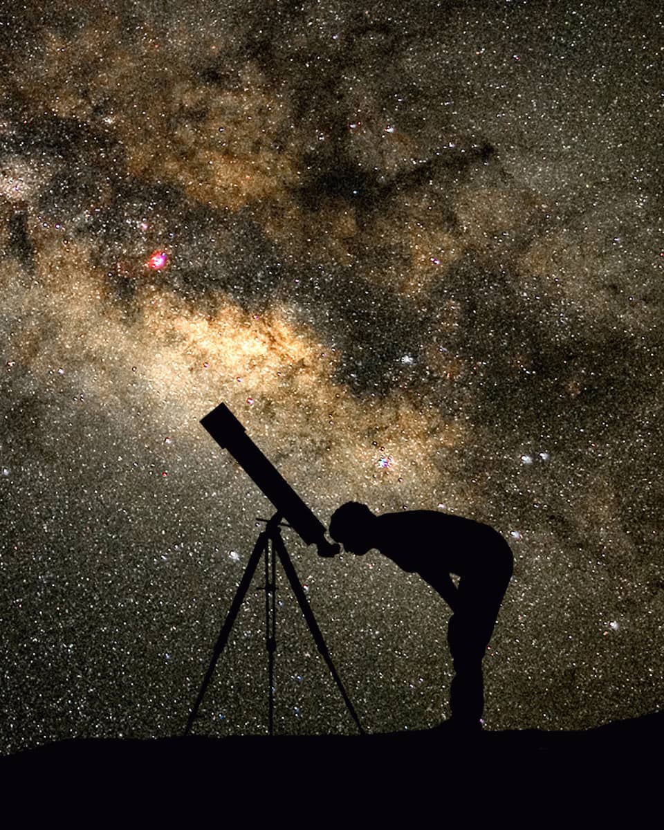 Silhouette of stargazer leaning into telescope against a starry sky, milky way