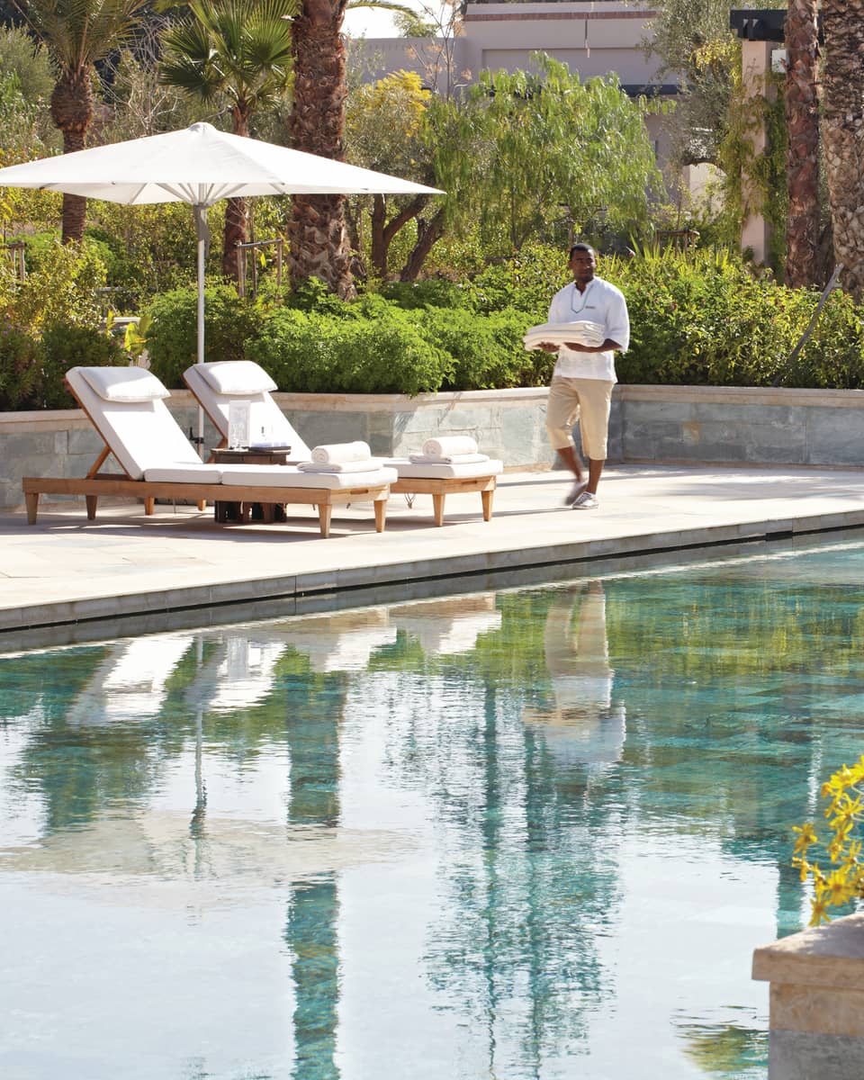 Server holding folded towels walks by lounge chairs, umbrella by adults-only outdoor swimming pool