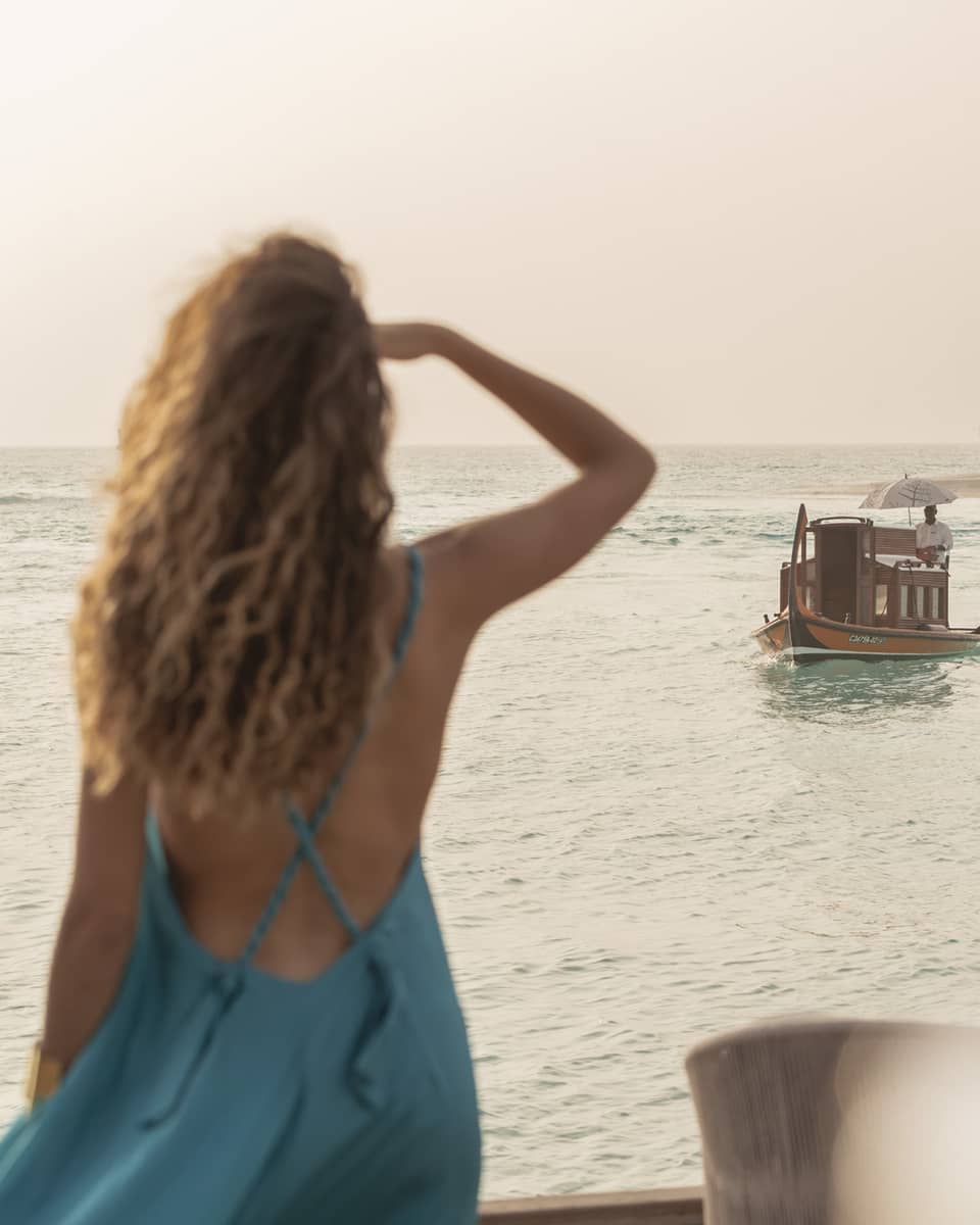 Person in blue dress shields eyes as boat travels toward shore