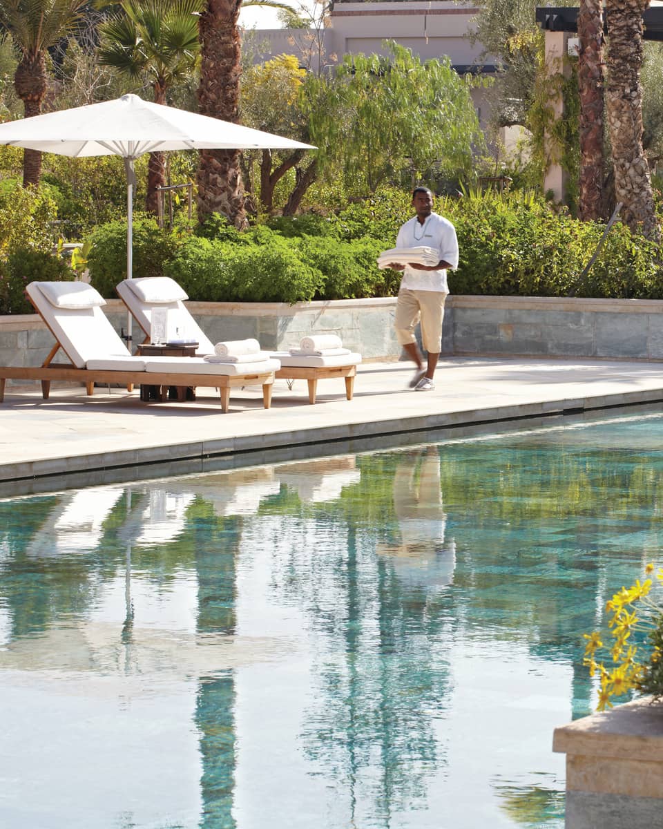 Server holding folded towels walks by lounge chairs, umbrella by adults-only outdoor swimming pool