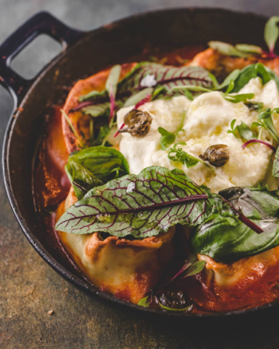 A pasta dish with a tomato sauce, and green leaves on top.