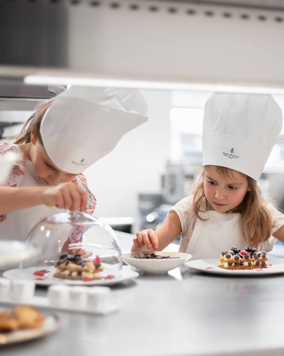 Two girls in chef hats making dessert in hotel kitchen