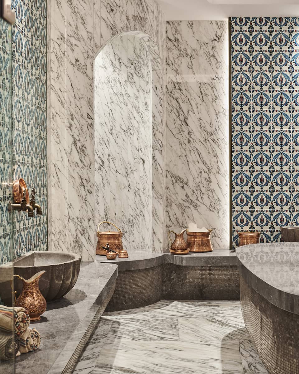 Steam shower with mosaic tile and full marble walls, floor and benches, and brass urns