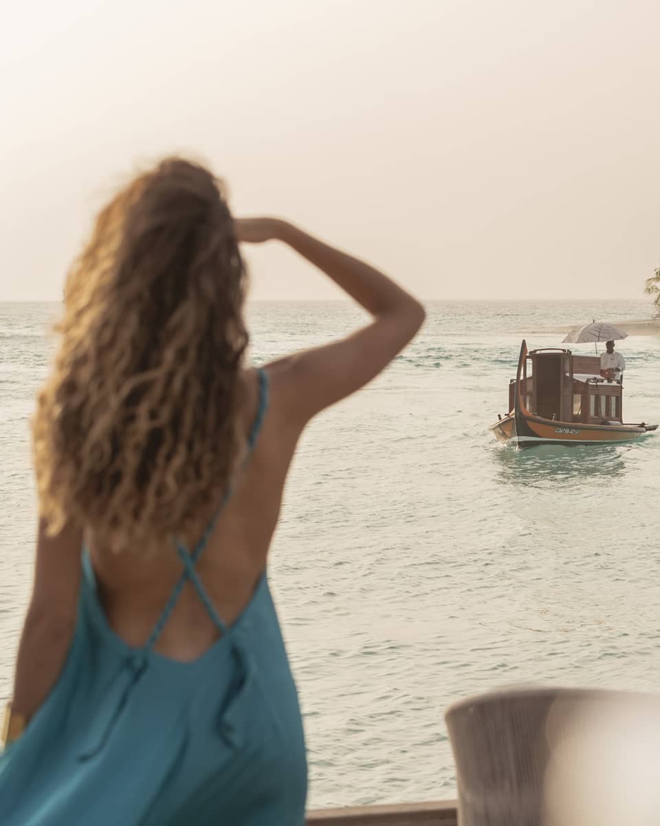 Person in blue dress shields eyes as boat travels toward shore
