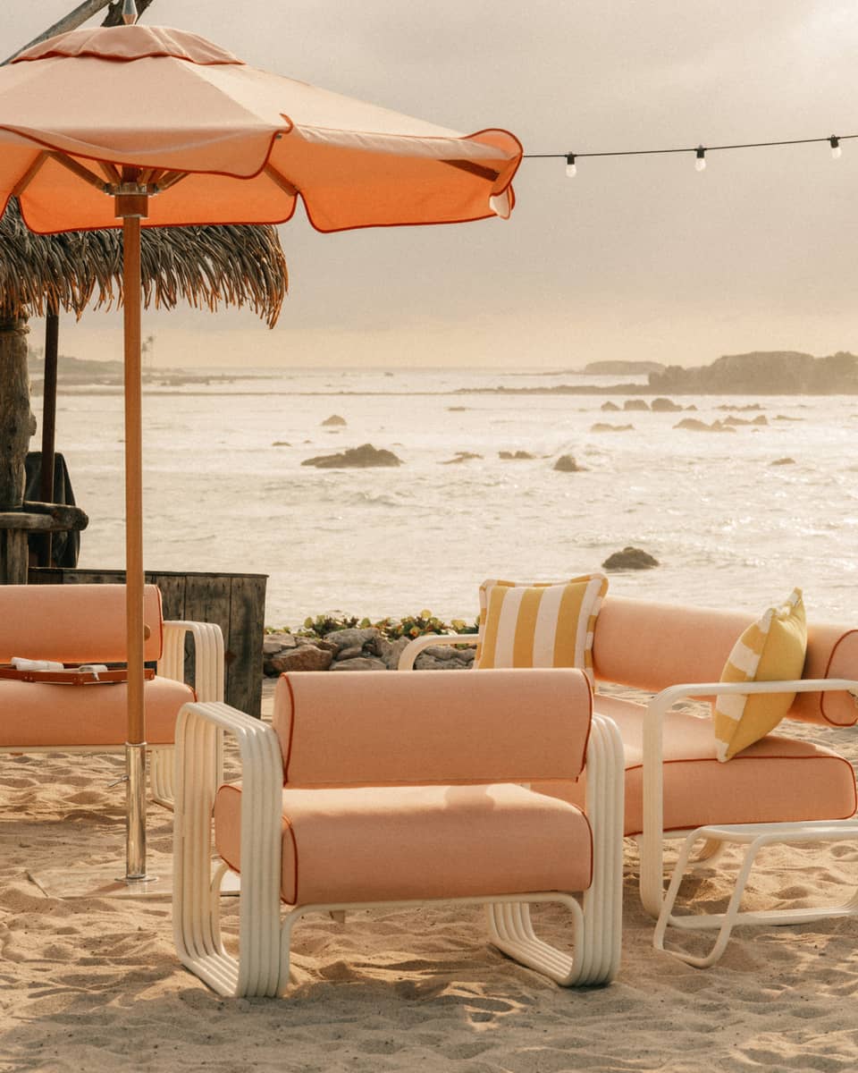 Light orange upholstered and fabric lounge chairs and sun umbrella on a beach with ocean and coastal views in the background