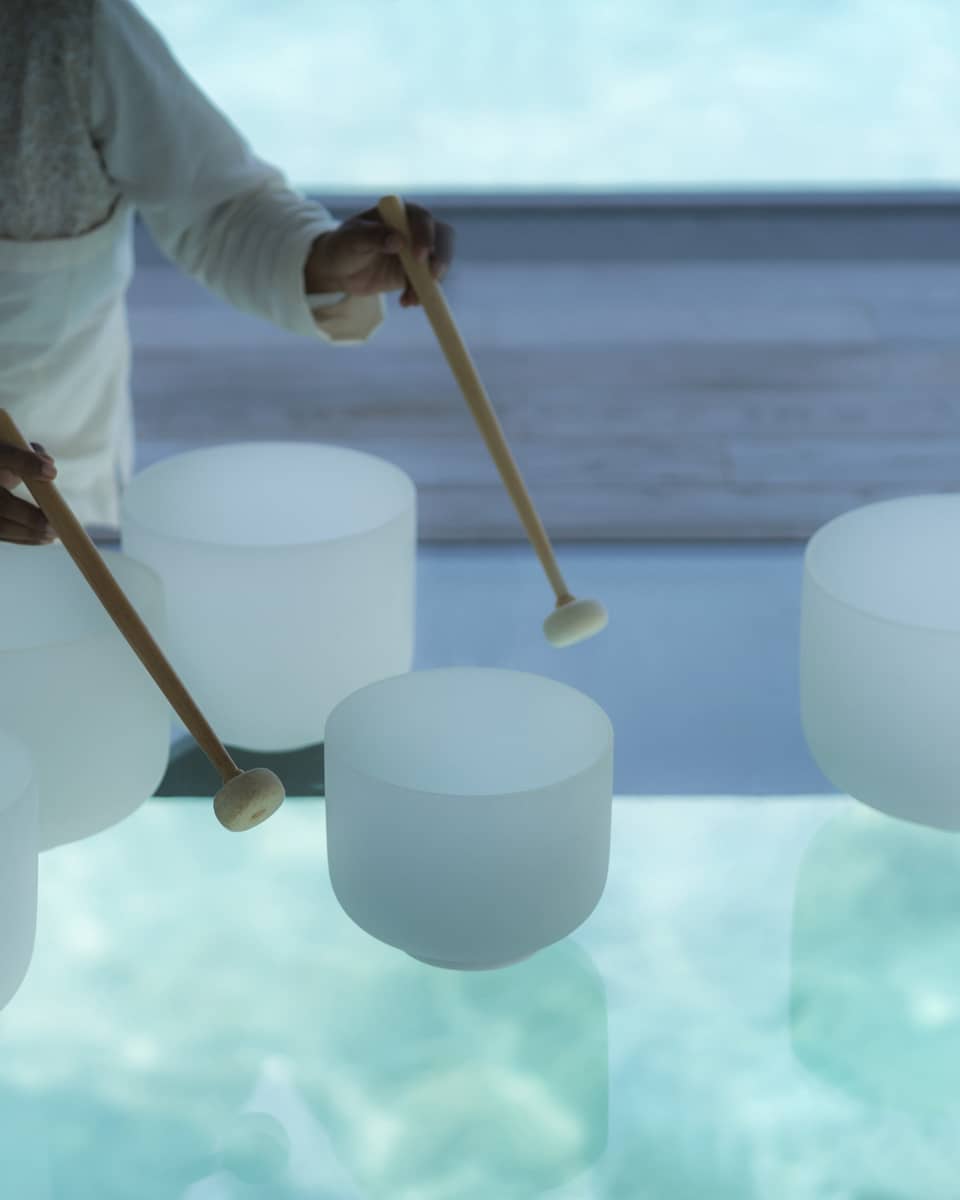 Spa staff plays various white crystal bowls with wood mallets during sound healing session