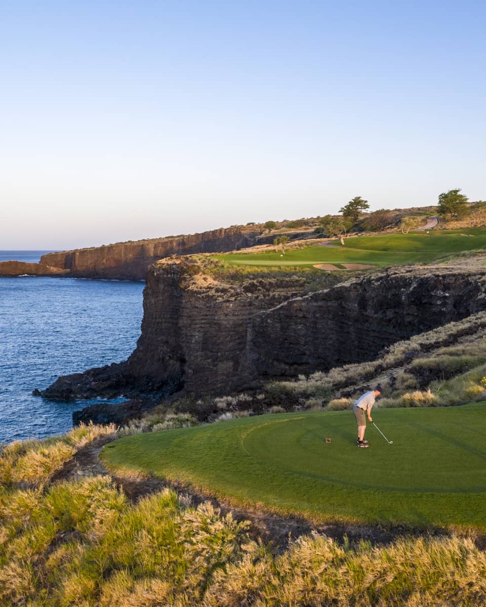Two golfers at the 12th-hole tee at Manele Golf Course at Four Seasons Resort Lanai, cliffs and ocean in background