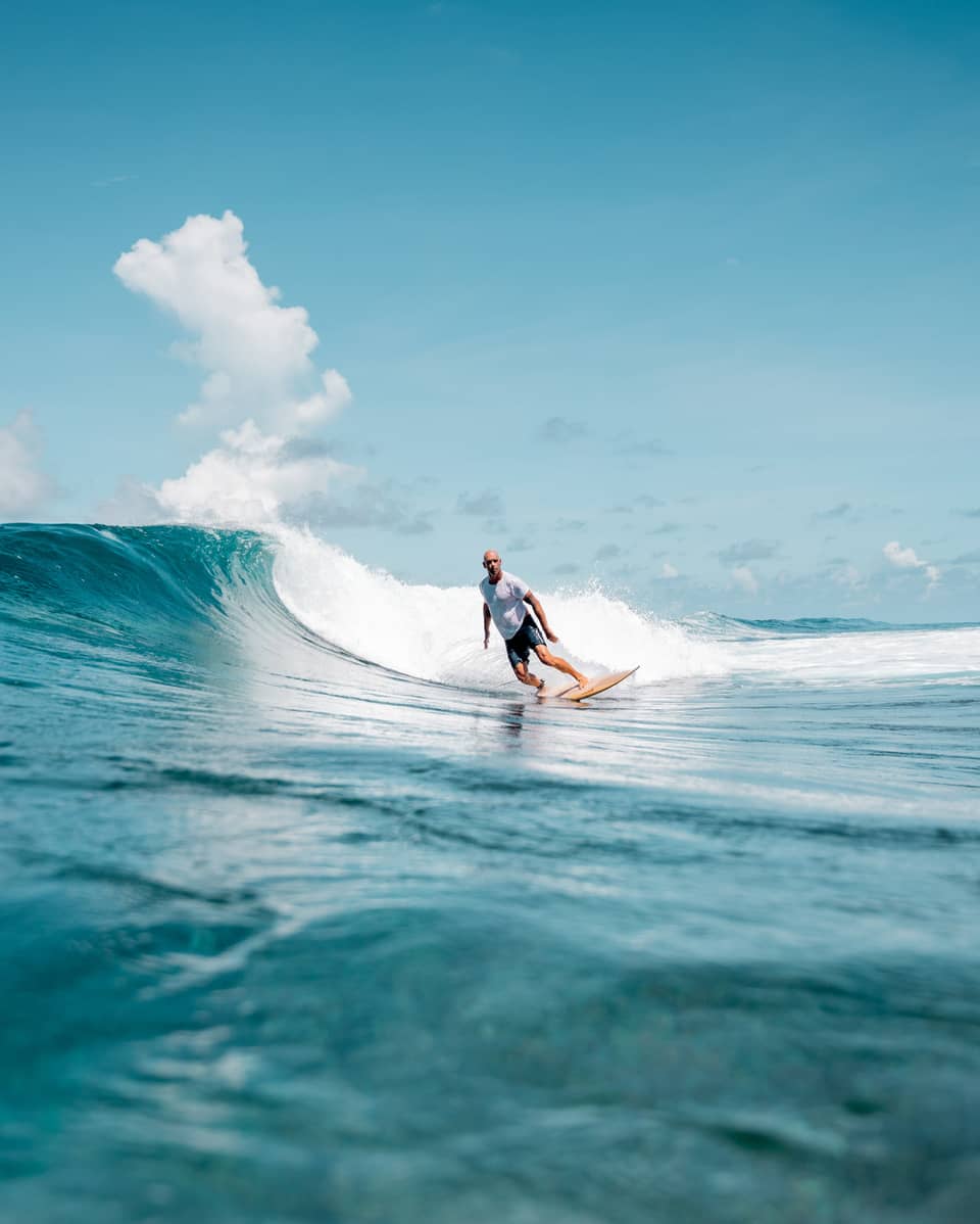 A person surfing a wave in the ocean, the water is a deep blue matched by the blue sky.