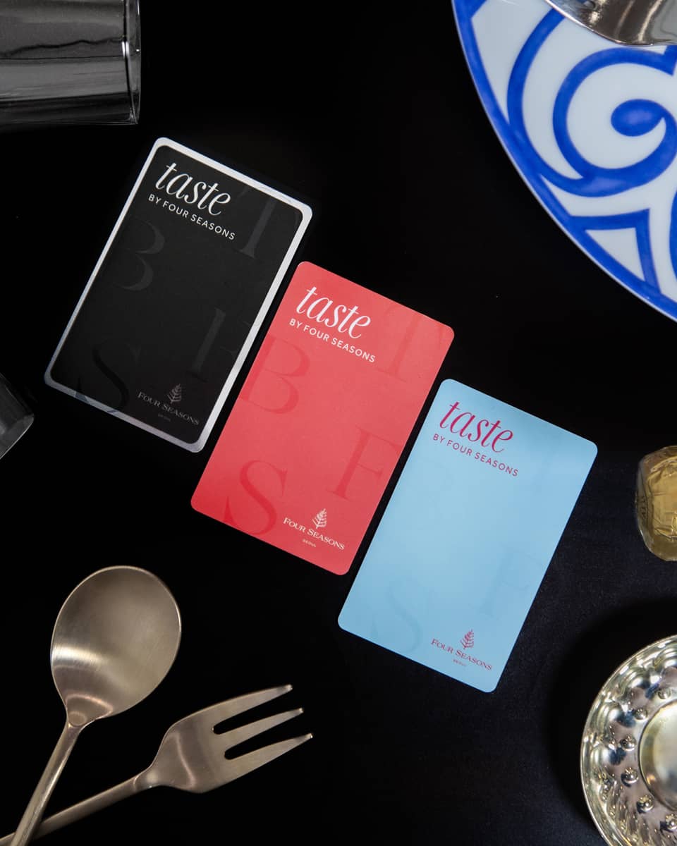 Three colours of Taste by Four Seasons cards on table with black tablecloth, stemmed wine glasses and silver cutlery