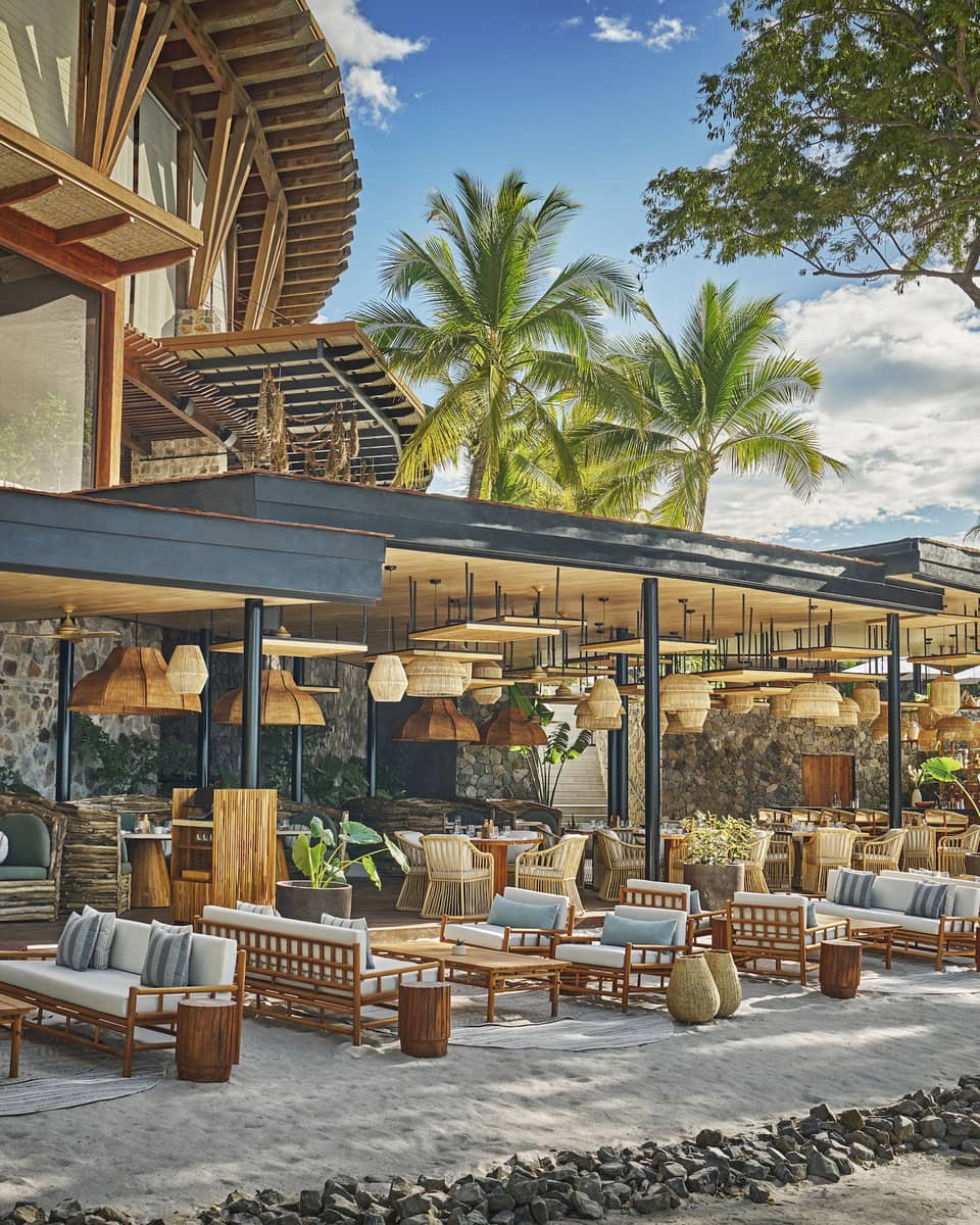 Tables, chairs and lounge seating set in groups on the sand along the edge of a reestaurant terrace