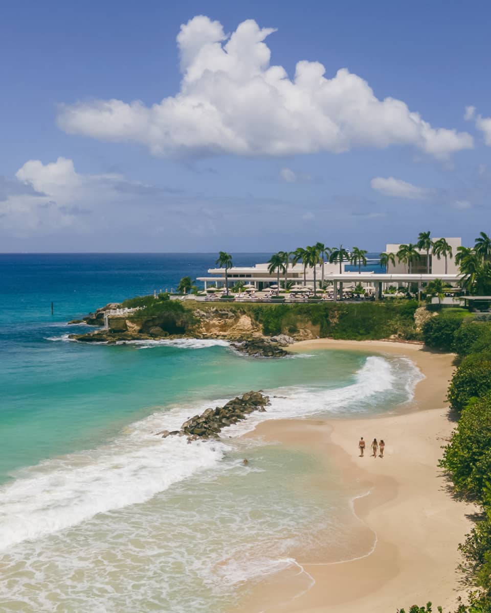 Turquoise waters and a sandy beach next to a verdant shore with structures nestled among the trees
