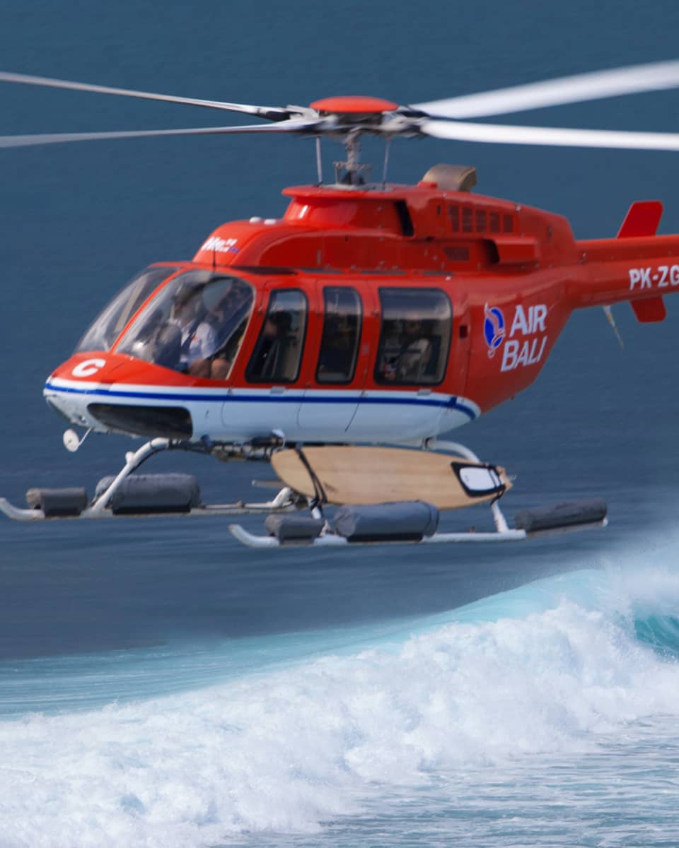 A helicopter hovers over the water for a guest to go helisurfing