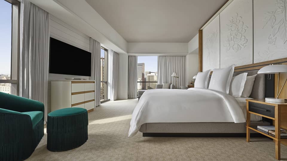 Suite with white king-size bed, flat screen TV, emerald green armchair and floor-to-ceiling windows