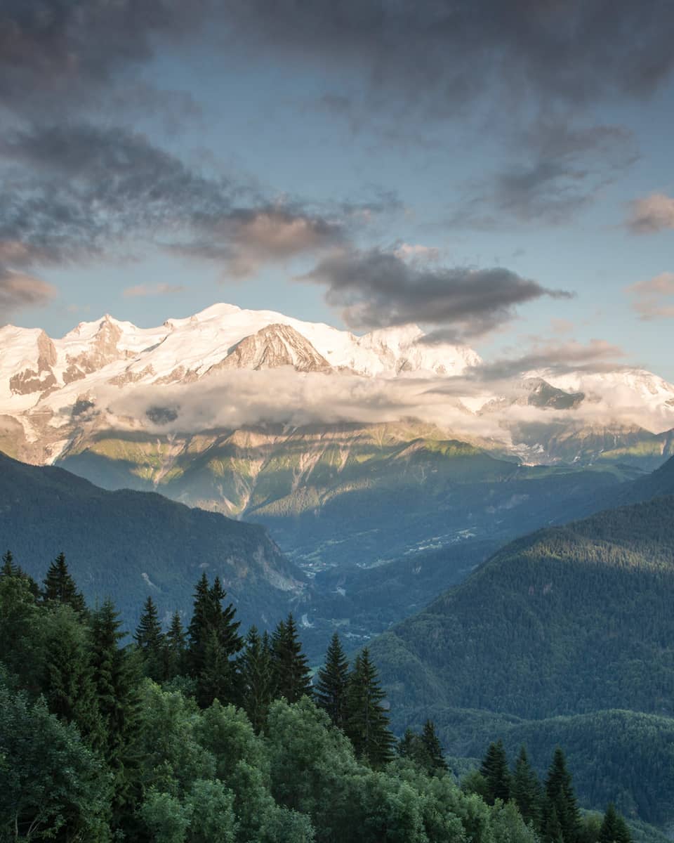 Clouds, sunshine over ice-capped French Alps behind green mountains