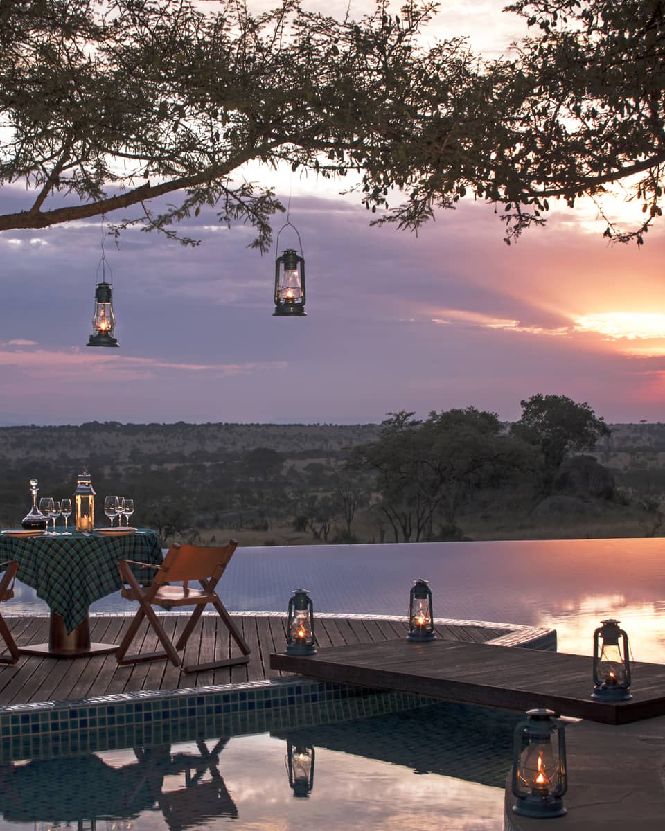 Private dining table on wood dock lined with lanterns, hanging from tree, sunset