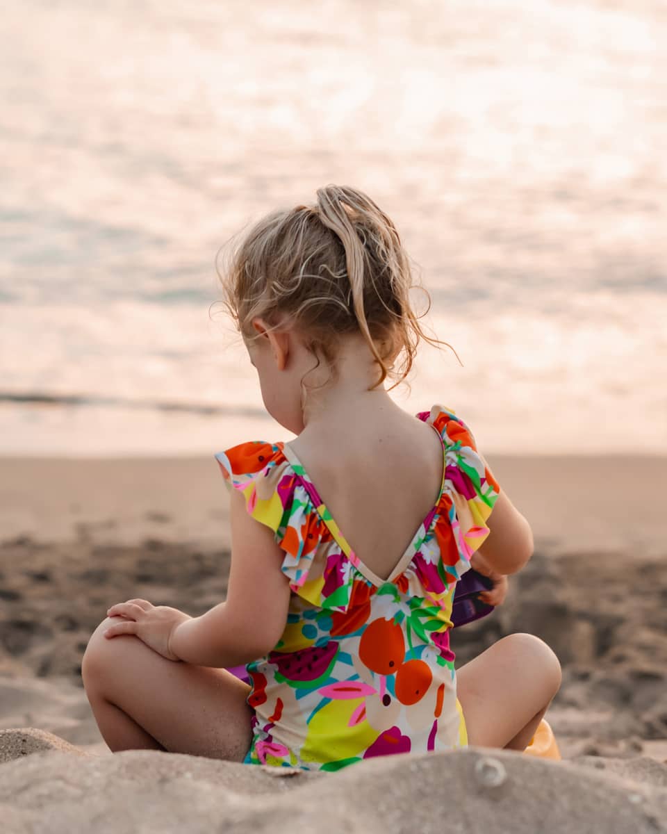 Young child sits on a sandy beach facing the water