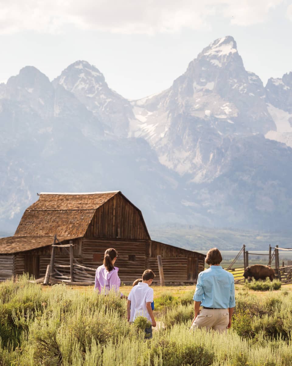 Family standing in a field with a cabin and mountains in the background.