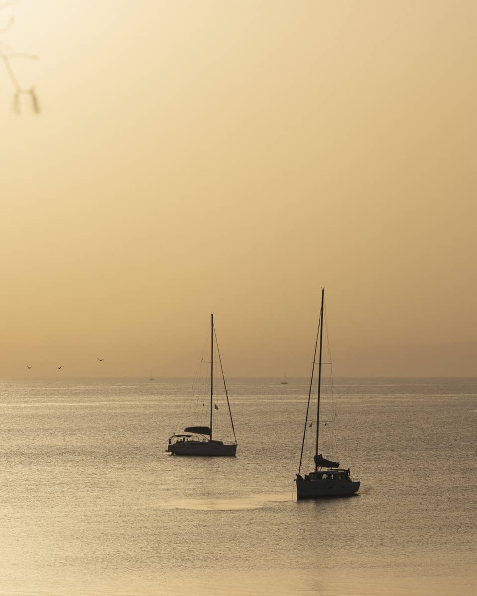 Silhouette of two sailboats at dusk on ocean cruising Greek isles.